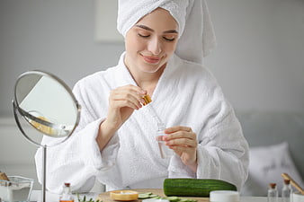 Woman in white robe applying skincare serum with dropper