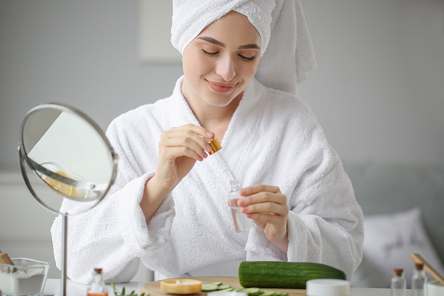 Woman in white robe applying skincare serum with dropper