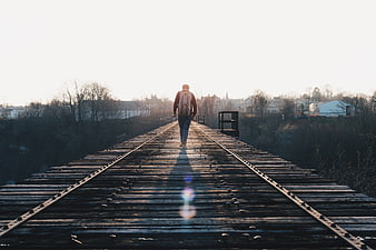 Man with backpack walking away on wooden railway bridge