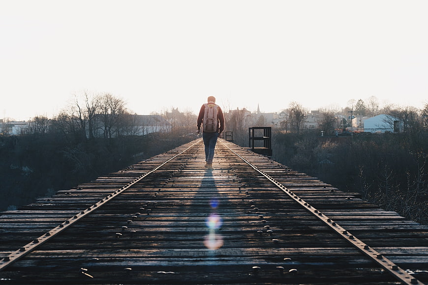 Man with backpack walking away on wooden railway bridge