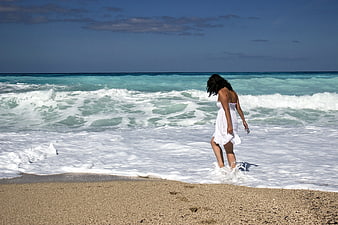 Woman in White Dress Walking in Ocean Waves on Sandy Beach