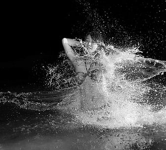 Woman splashing in water with flowing fabric in black and white