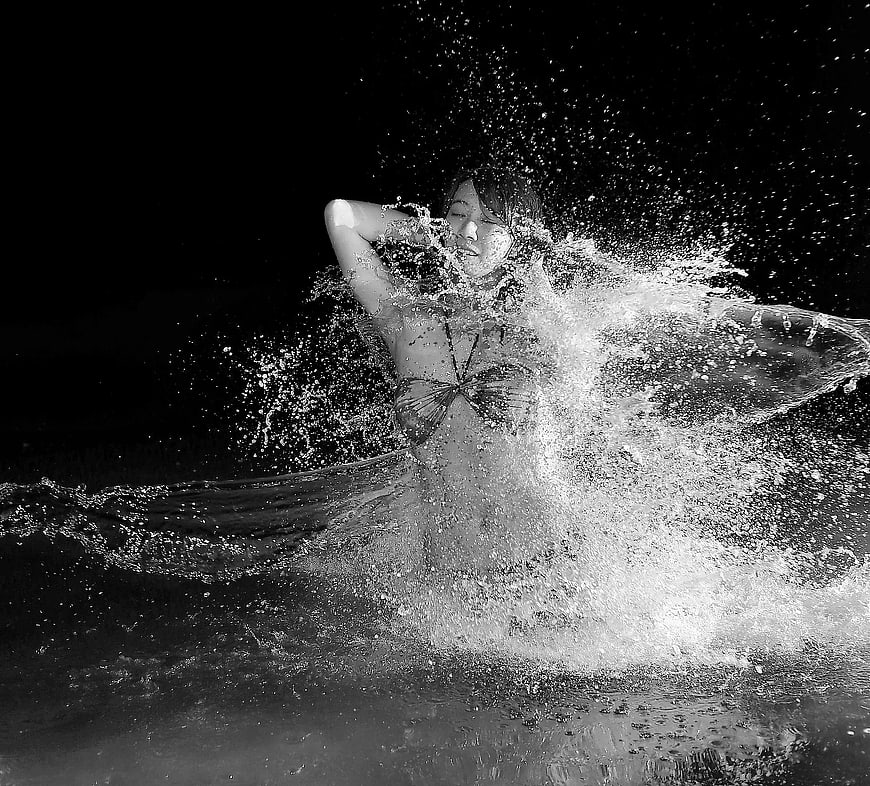 Woman splashing in water with flowing fabric in black and white