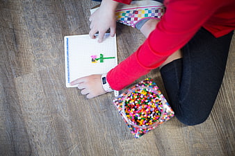 Child making bead art on wooden floor