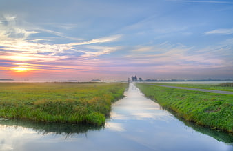 Misty Canal at Sunrise with Colorful Sky and Green Fields