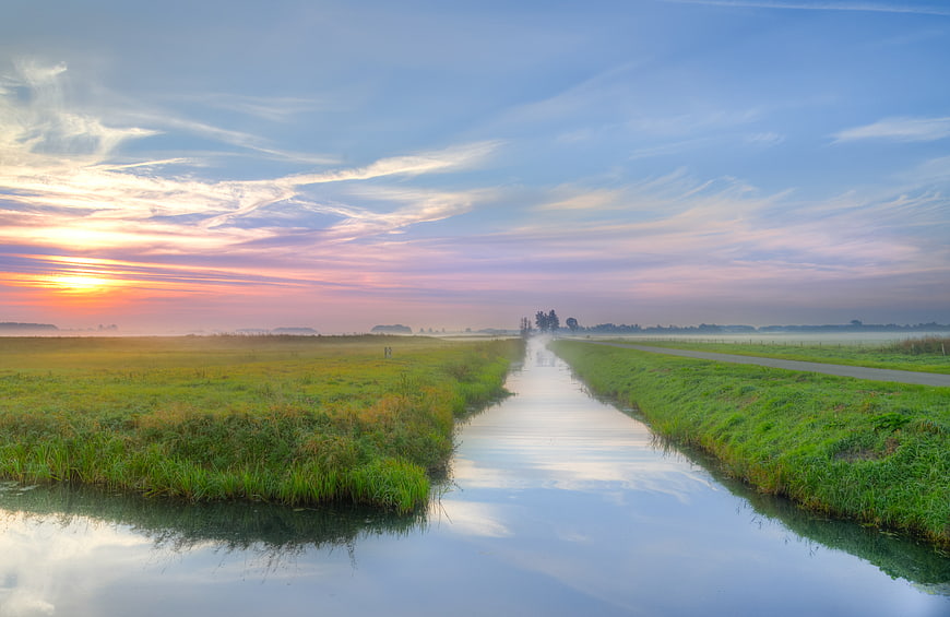 Misty Canal at Sunrise with Colorful Sky and Green Fields