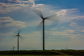 Wind turbines spinning in a green field under a cloudy blue sky