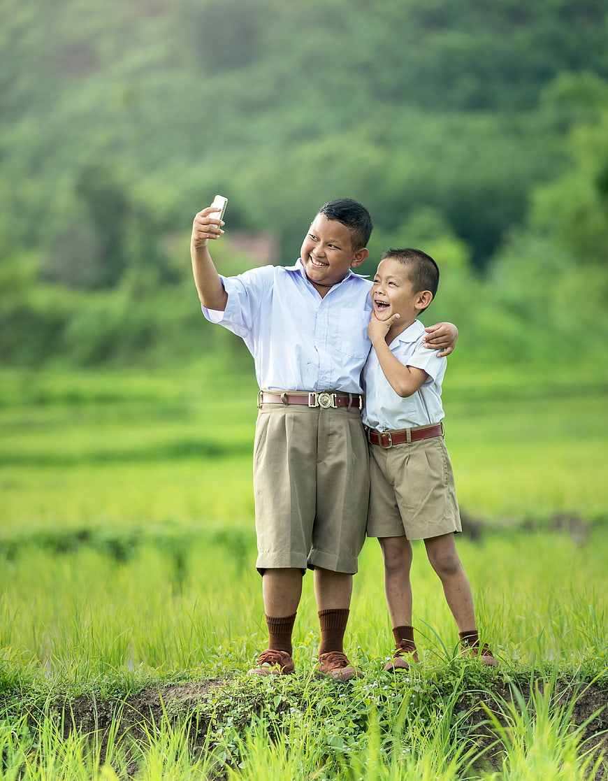 Two Schoolboys Taking a Joyful Selfie in a Green Rice Paddy Field