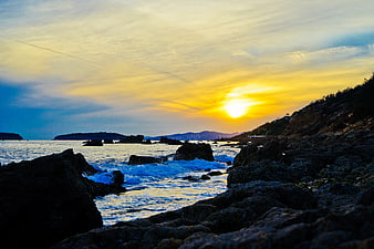 Golden Sunset Over Rocky Coastal Shoreline with Ocean Waves