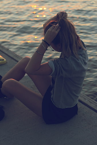 Woman sitting by water at sunset fixing hair