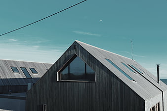 Modern wooden house roof with triangular window against blue sky