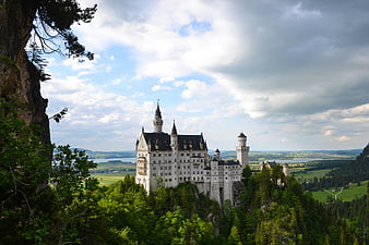 Neuschwanstein Castle on Rocky Hill with Green Forest and Cloudy Sky