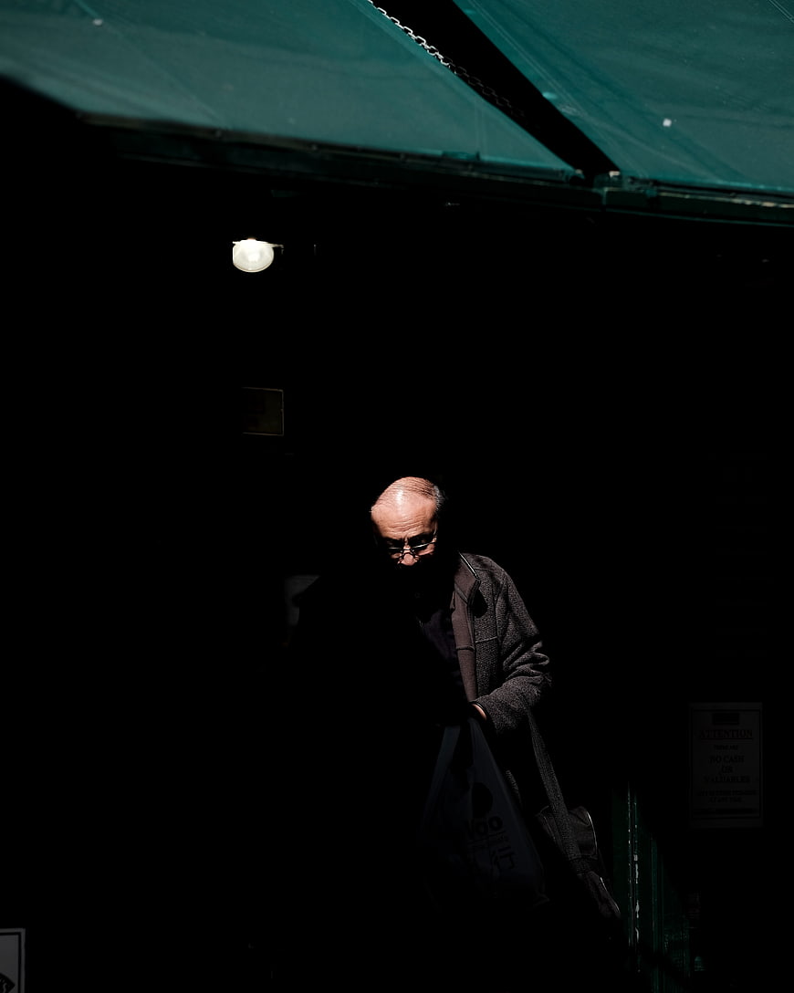 Old man walking in shadows under green awning