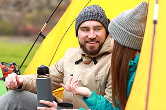 Happy couple camping in yellow tent with thermos
