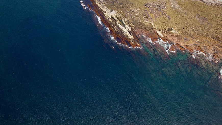Aerial View of Rugged Coastline Meeting Deep Blue Ocean