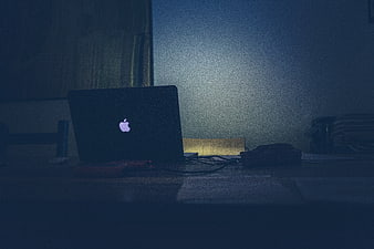 Dark moody laptop on desk at night with glowing logo