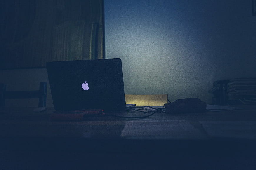 Dark moody laptop on desk at night with glowing logo