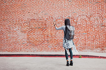 Woman taking selfie against red brick wall
