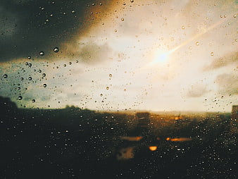 Raindrops on window glass with blurred city sunset background