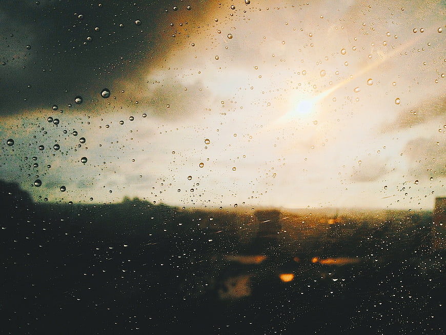 Raindrops on window glass with blurred city sunset background