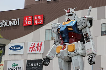 Giant Gundam Statue Standing In Front Of Shopping Mall Storefronts