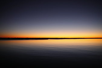 Serene Sunset Over Calm Water with Orange and Blue Sky Gradient