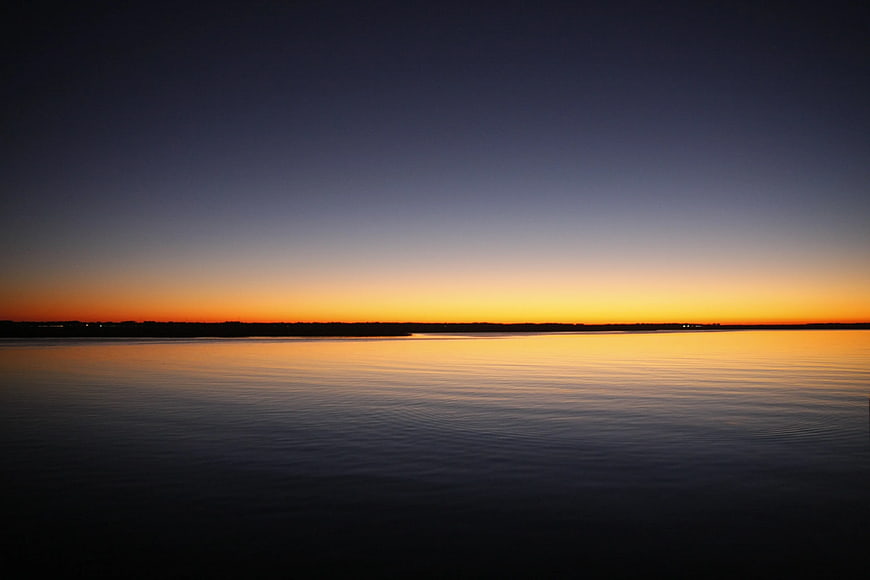 Serene Sunset Over Calm Water with Orange and Blue Sky Gradient