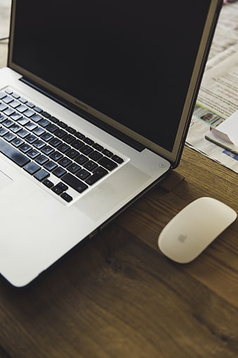 Silver laptop and white mouse on wooden desk with newspaper
