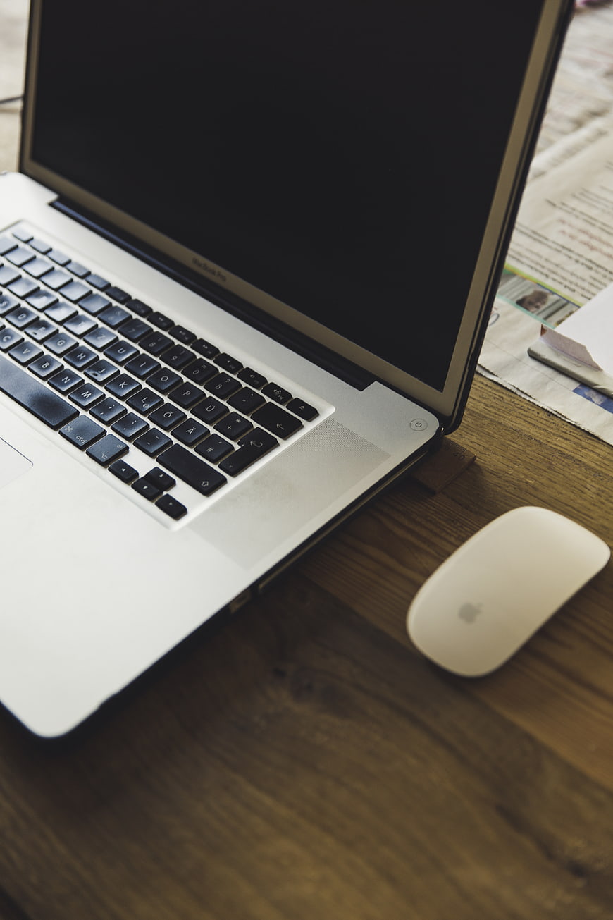 Silver laptop and white mouse on wooden desk with newspaper