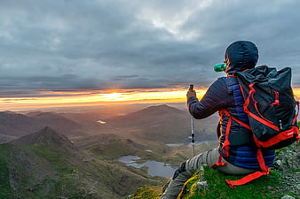 Hiker on Mountain Peak Watching Dramatic Sunrise Over Valley