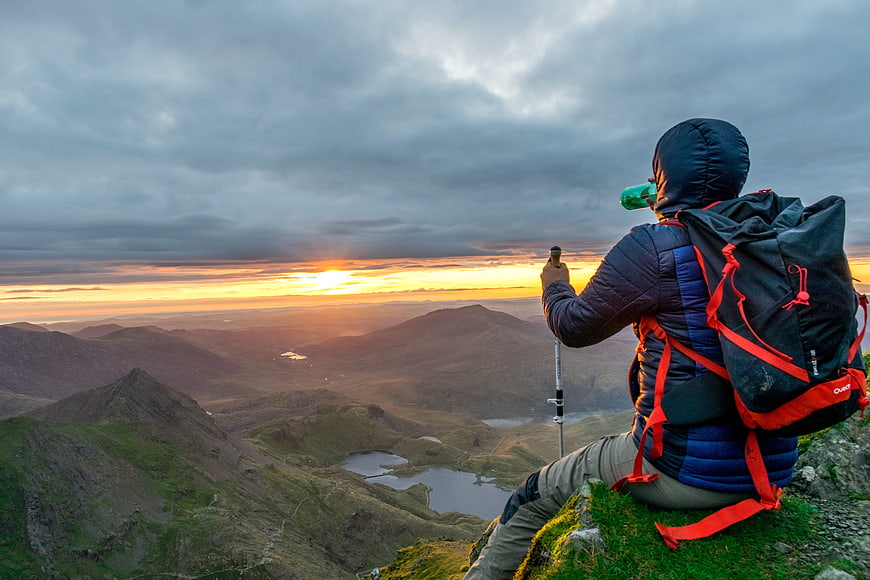 Hiker on Mountain Peak Watching Dramatic Sunrise Over Valley