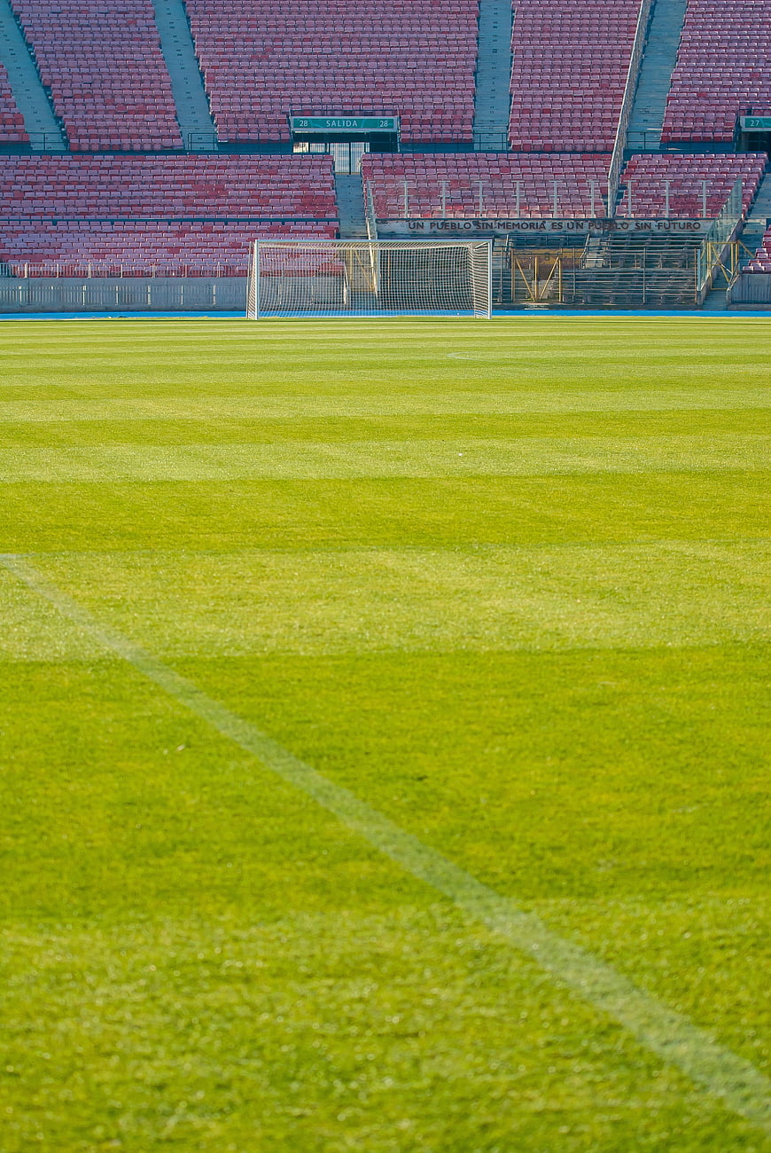 Empty soccer stadium with green grass field and red seats