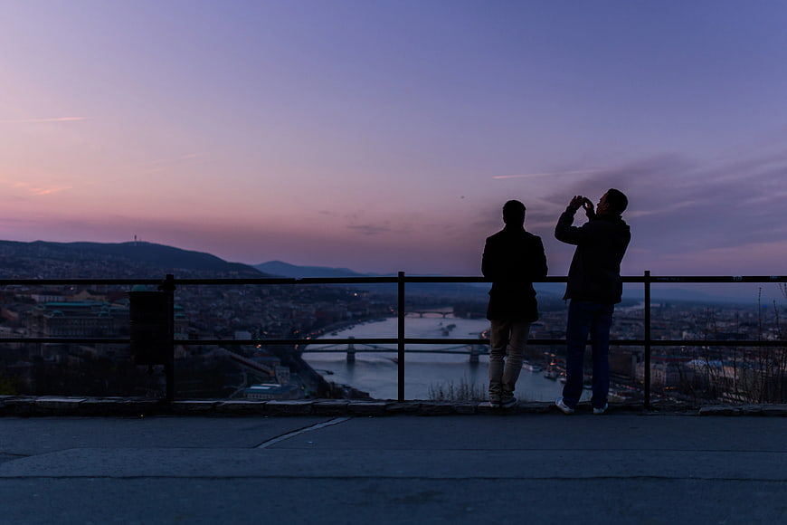 Silhouettes of Two People Taking Photos at Sunset Over City