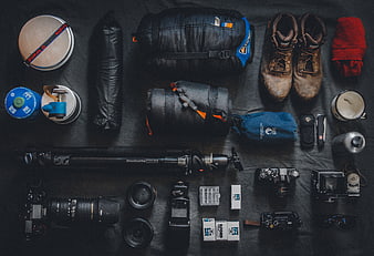 Flat lay of hiking and photography gear on dark background