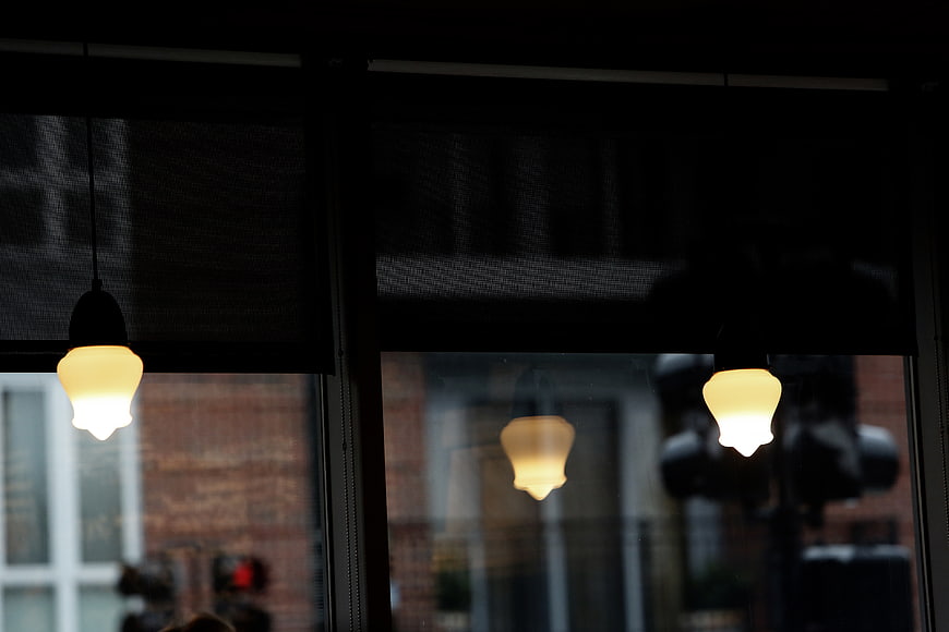 Warm pendant lights reflected in a dark cafe window