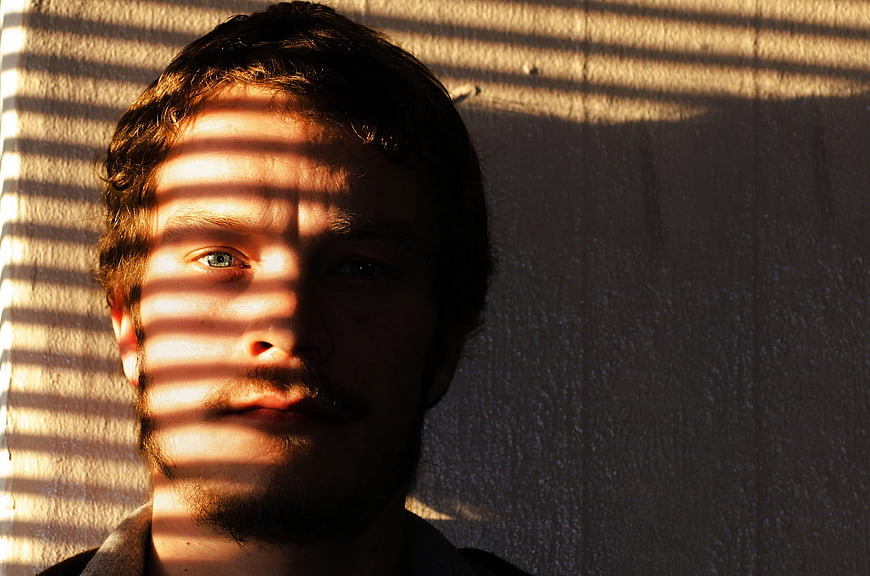Man's face with striped shadows from blinds