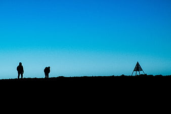 Silhouettes of Hikers on Highland Ridge Against Blue Sky