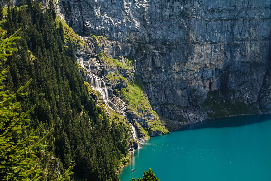 Turquoise alpine lake with cascading waterfall and pine forest