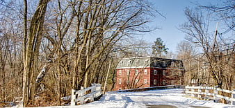 Red brick millhouse in winter with snow-covered road and white fence