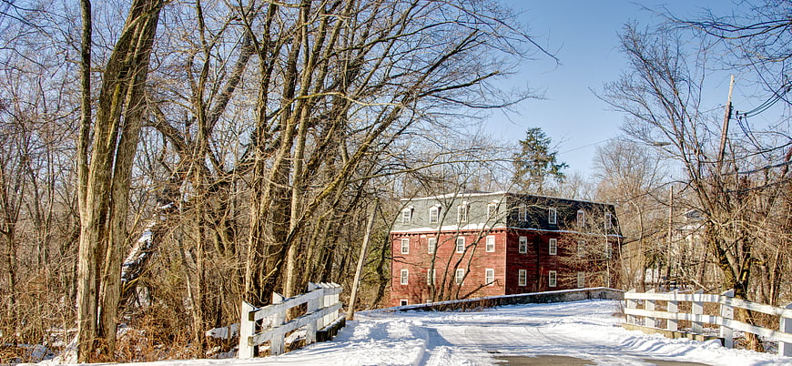 Red brick millhouse in winter with snow-covered road and white fence