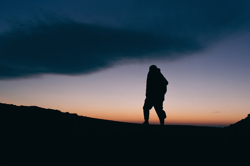 Silhouette of Hiker Walking on Mountain Ridge at Sunset