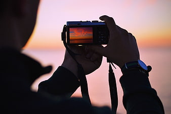 Photographer capturing sunset with digital camera