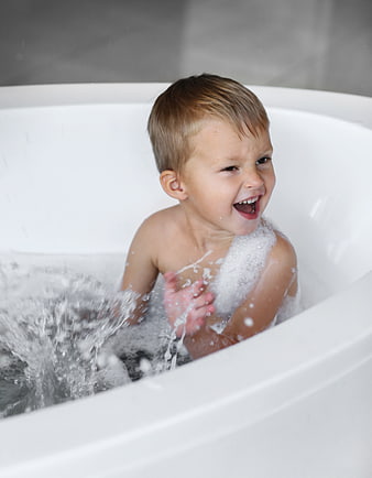 Happy Toddler Boy Splashing in Bathtub with Bubbles