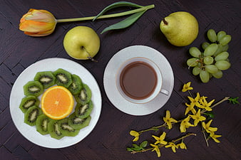 Overhead view of coffee, kiwi, orange, and spring flowers on dark wood
