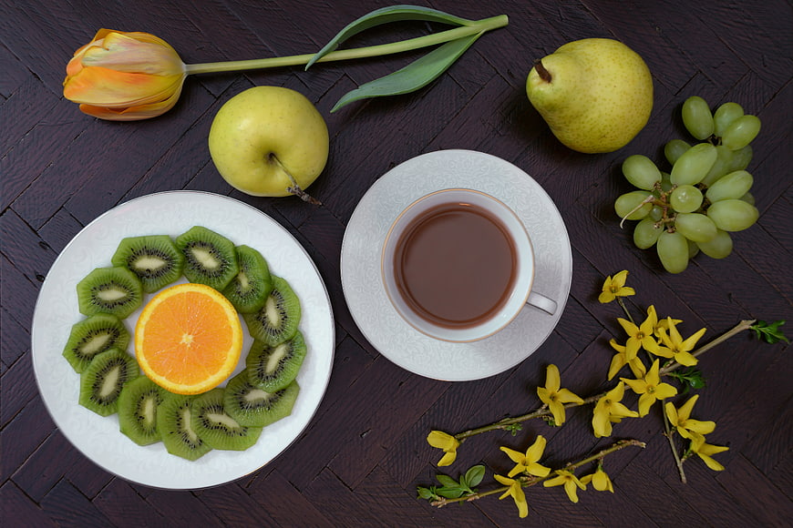 Overhead view of coffee, kiwi, orange, and spring flowers on dark wood