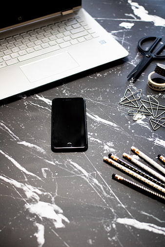 Flat lay of smartphone, laptop, and stationery on marble desk