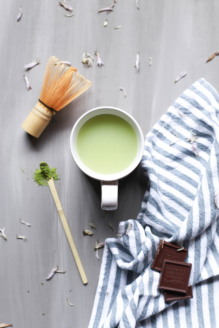 Top view of matcha latte with whisk and chocolate
