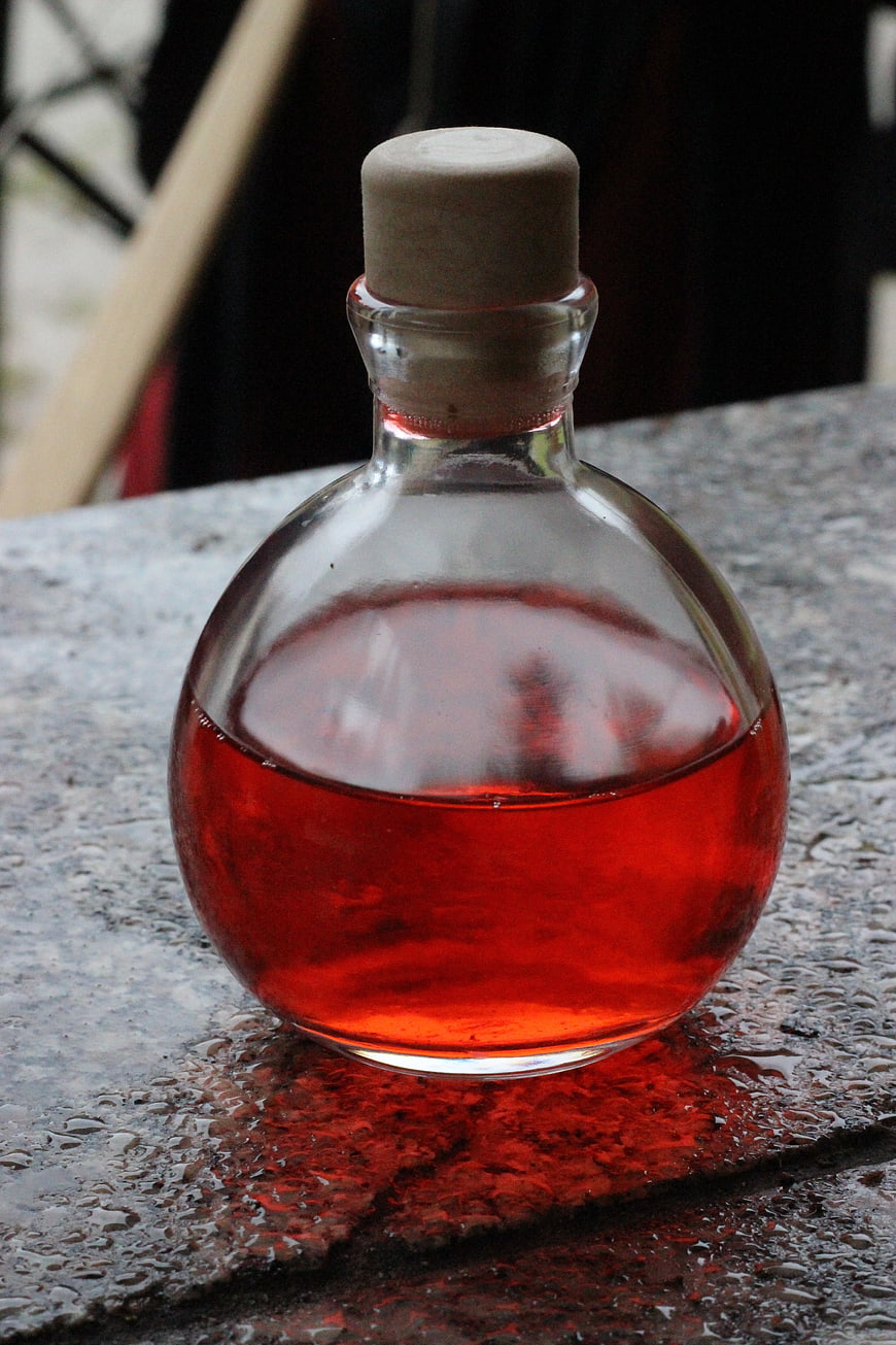 Round glass bottle with red liquid and cork stopper on wet stone surface