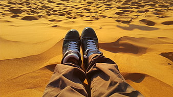 First-person view of sneakers on golden desert sand dunes