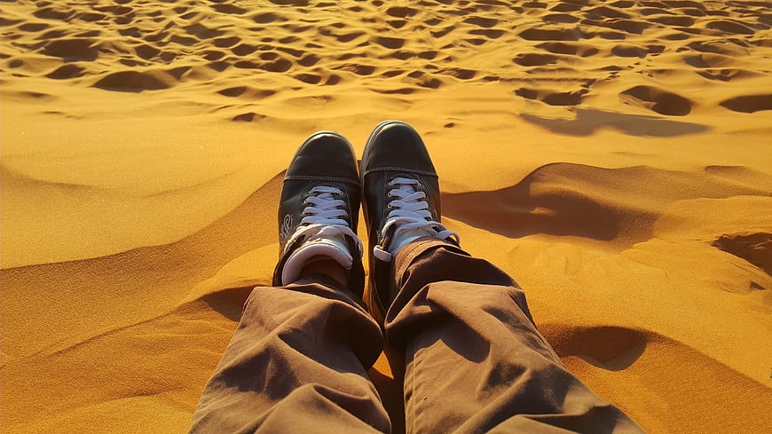 First-person view of sneakers on golden desert sand dunes